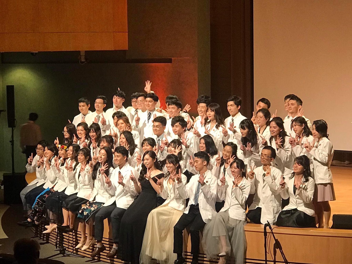 Group photo of students dressed in white robes. The right hand shows 1 and the left hand shows 4, to symbolize CM114.